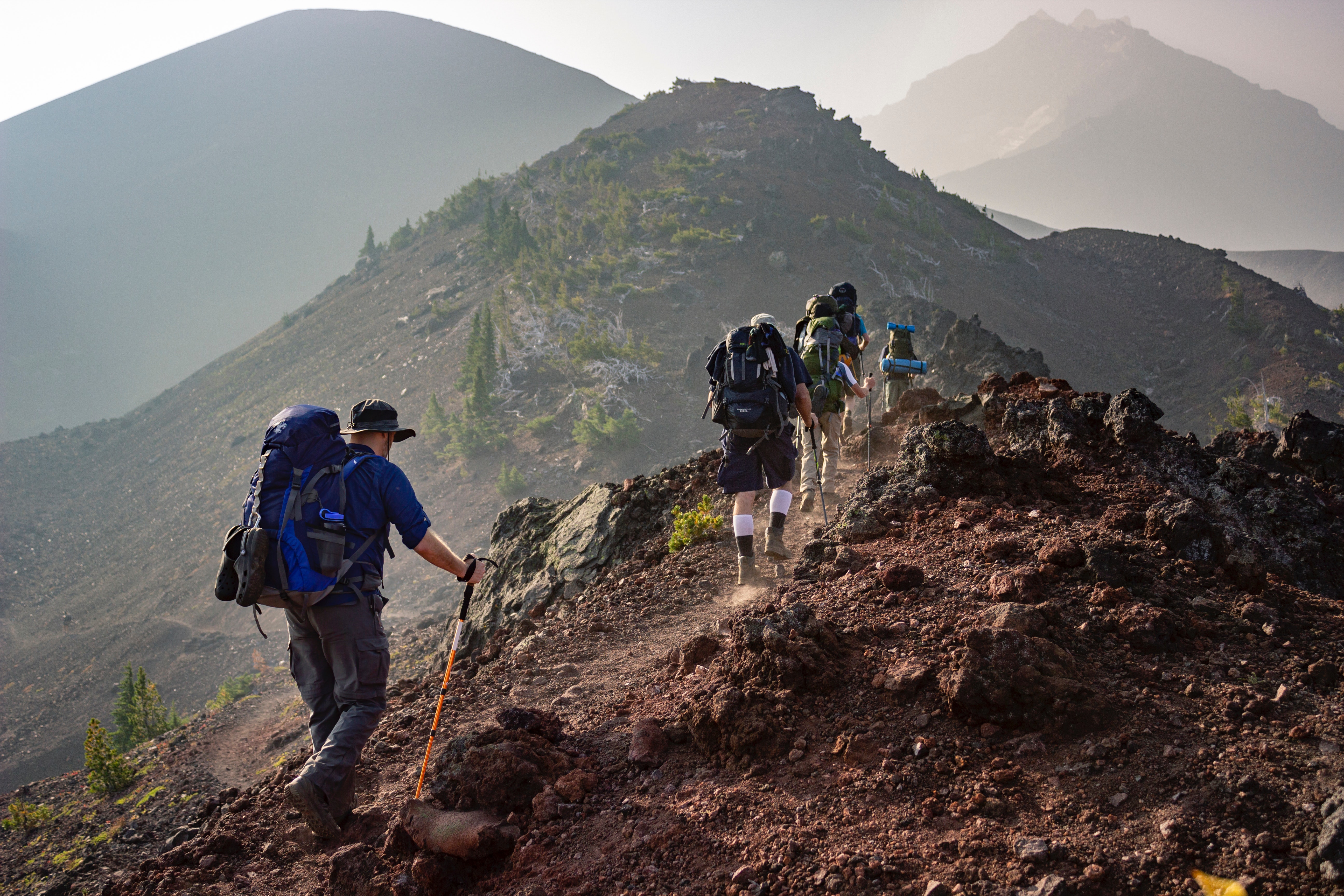 three people hiking mountains on a trail with backpacking gear and trekking poles