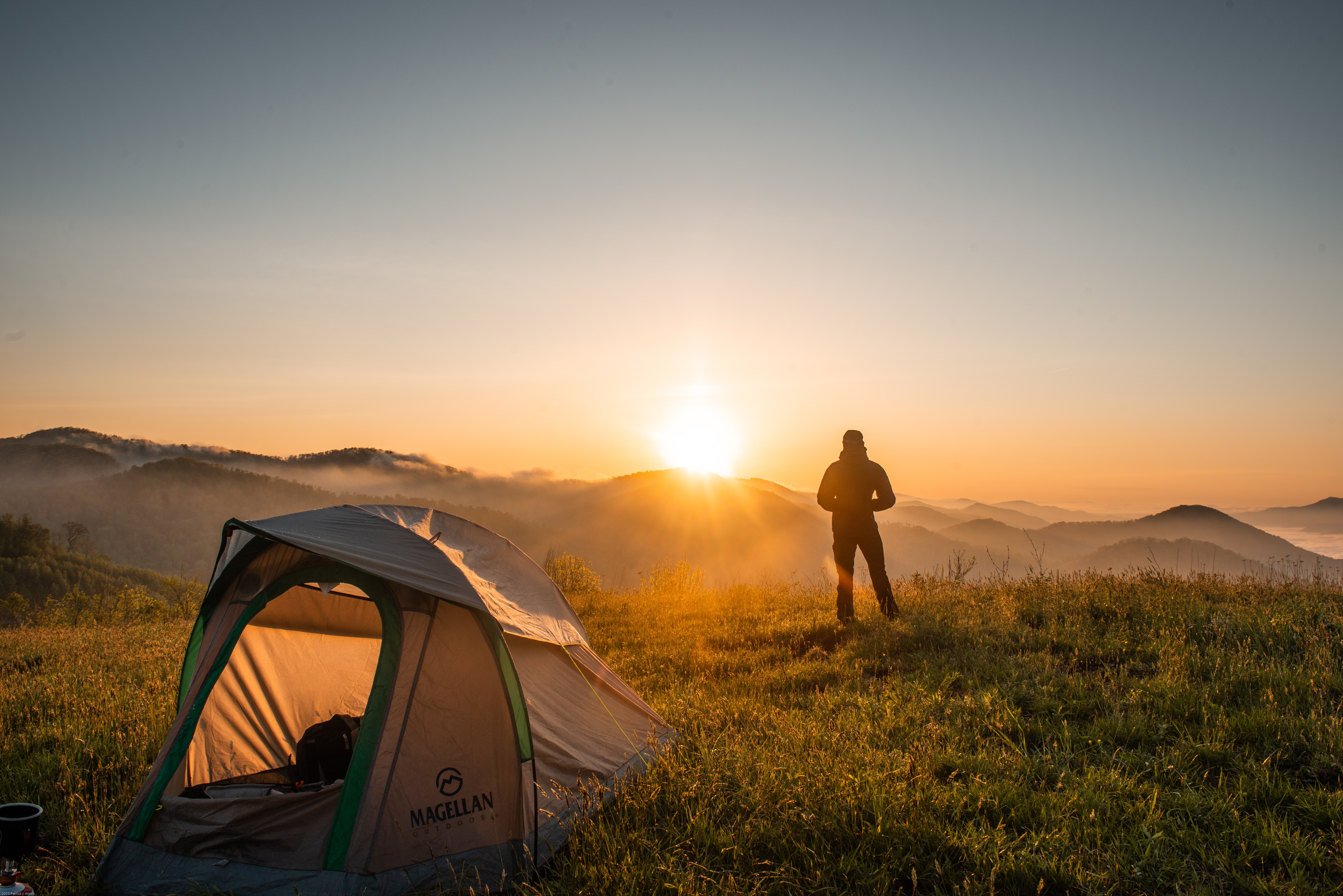 a person standing on top of a hill watching the sunset next to their tent